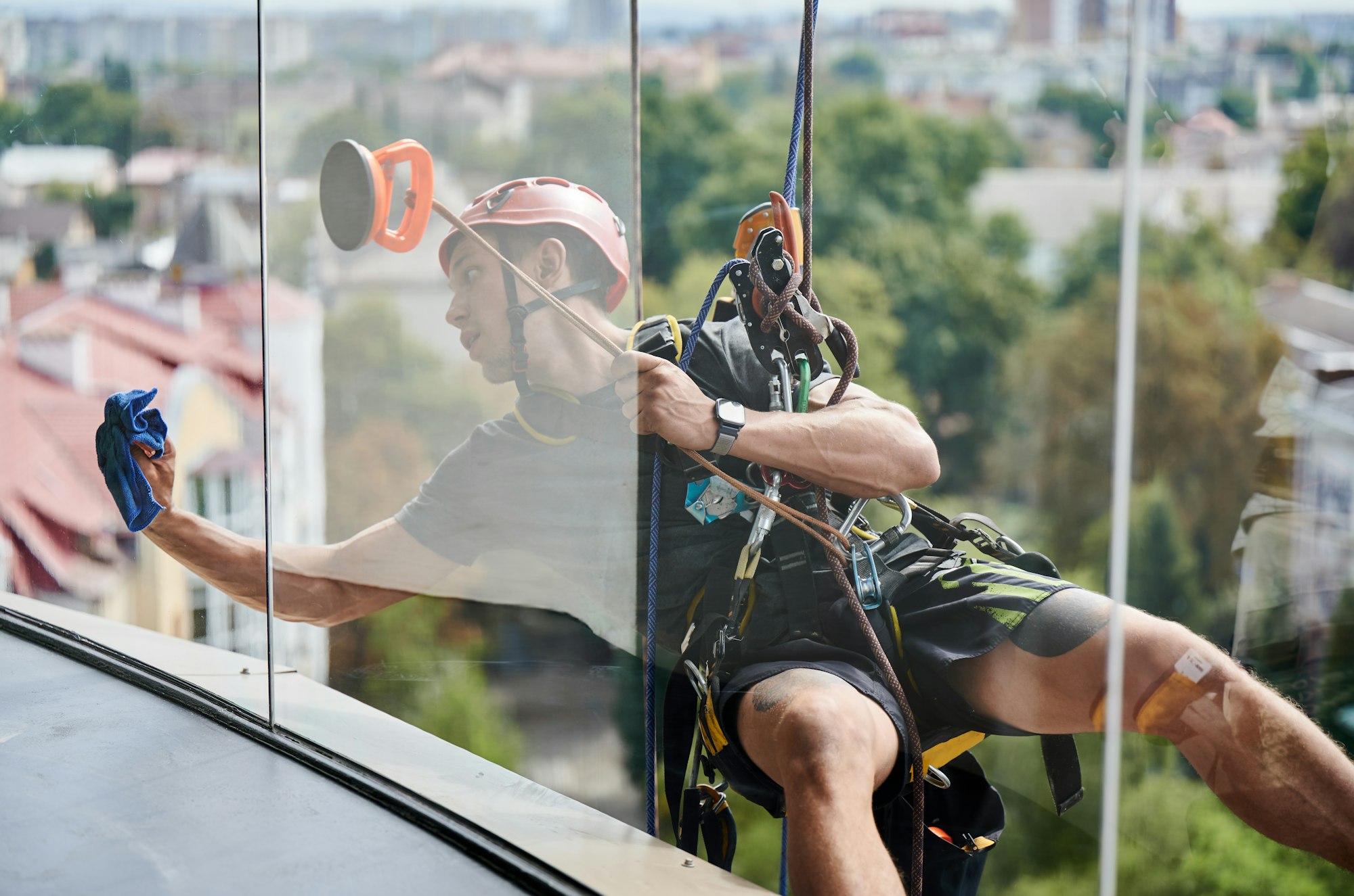 Industrial mountaineering worker cleaning window outside building.